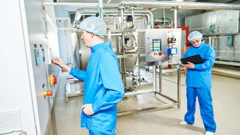 Two people in blue lab coats operating machinery in a laboratory setting