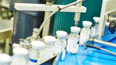 A machine filling small glass bottles with clear liquid in a laboratory setting